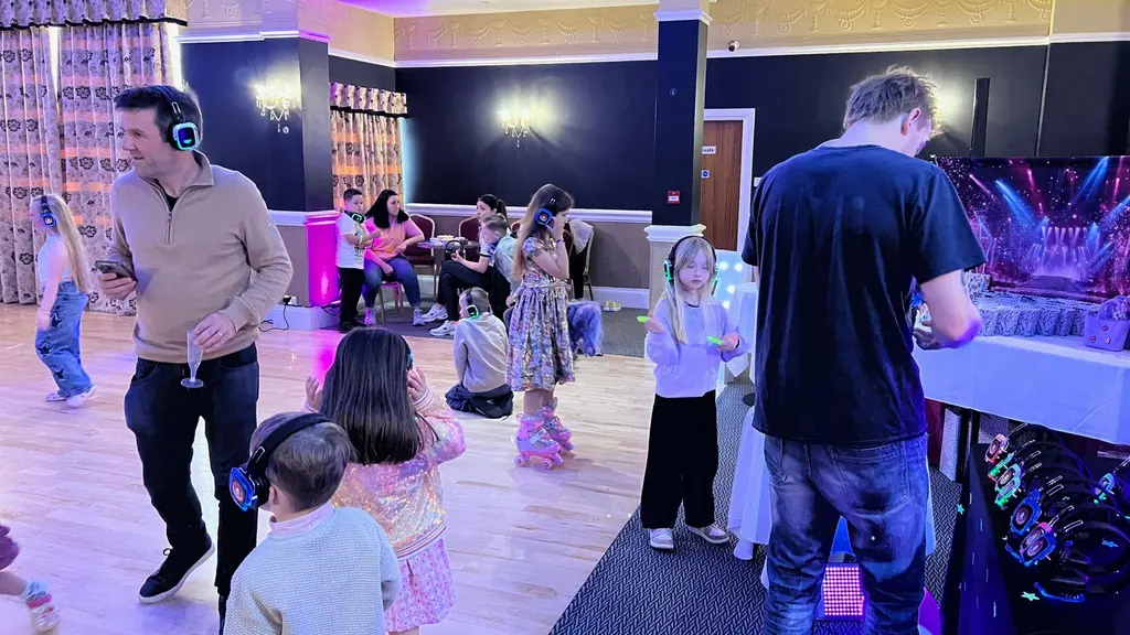 Children and adults in silent disco headphones dancing at a party in a hall.