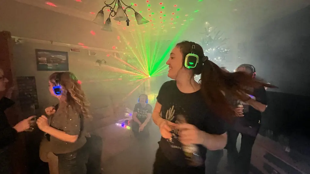 Two women in glowing headphones dancing at a silent disco, with green laser lights behind them.